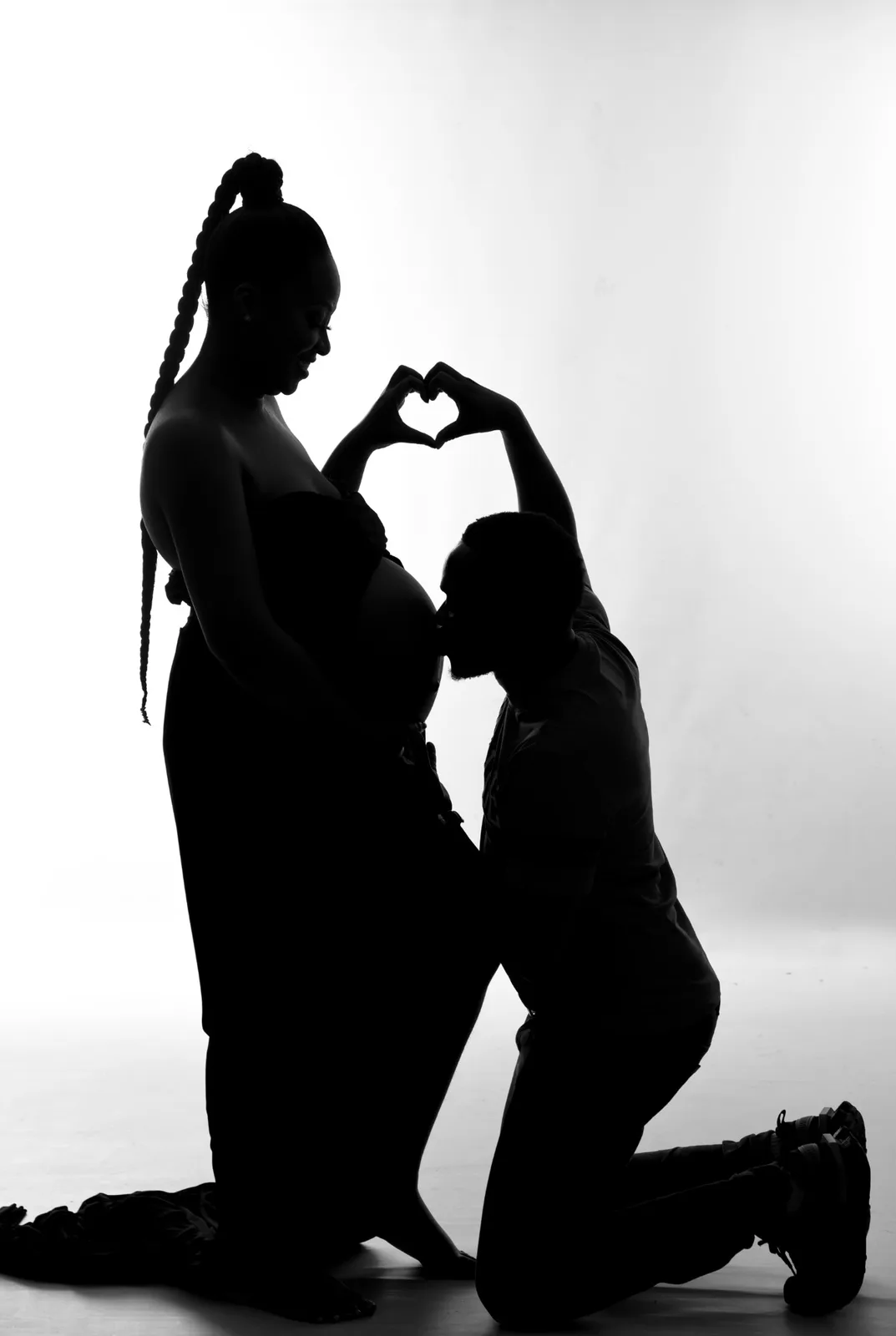 Silhouette of a father-to-be kissing the baby bump while making a heart with his hands